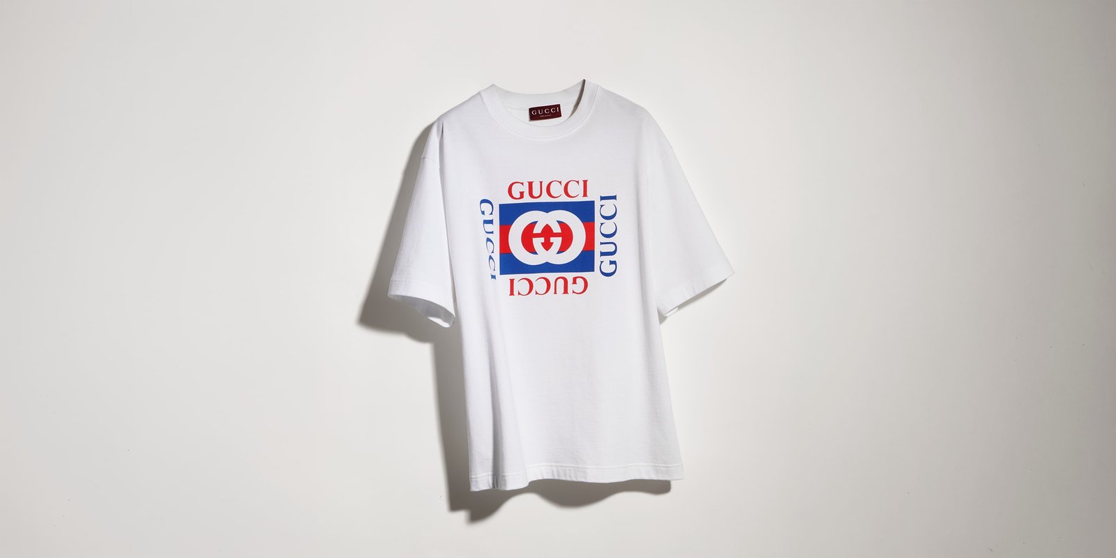 White cotton logo T-shirt displayed against a plain wall.