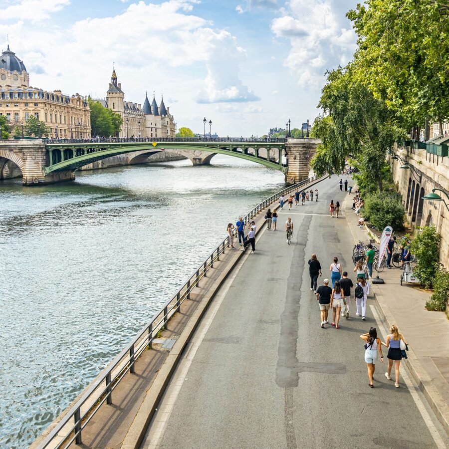 Visitors strolling along a broad Paris riverside path.