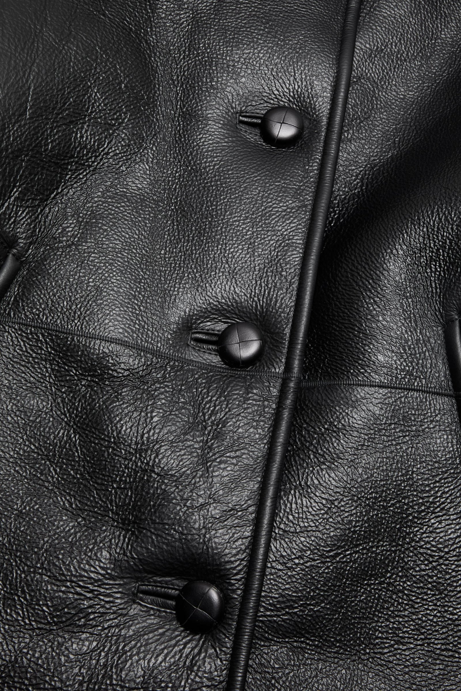 Smooth leather exterior and button closure on shearling outerwear.