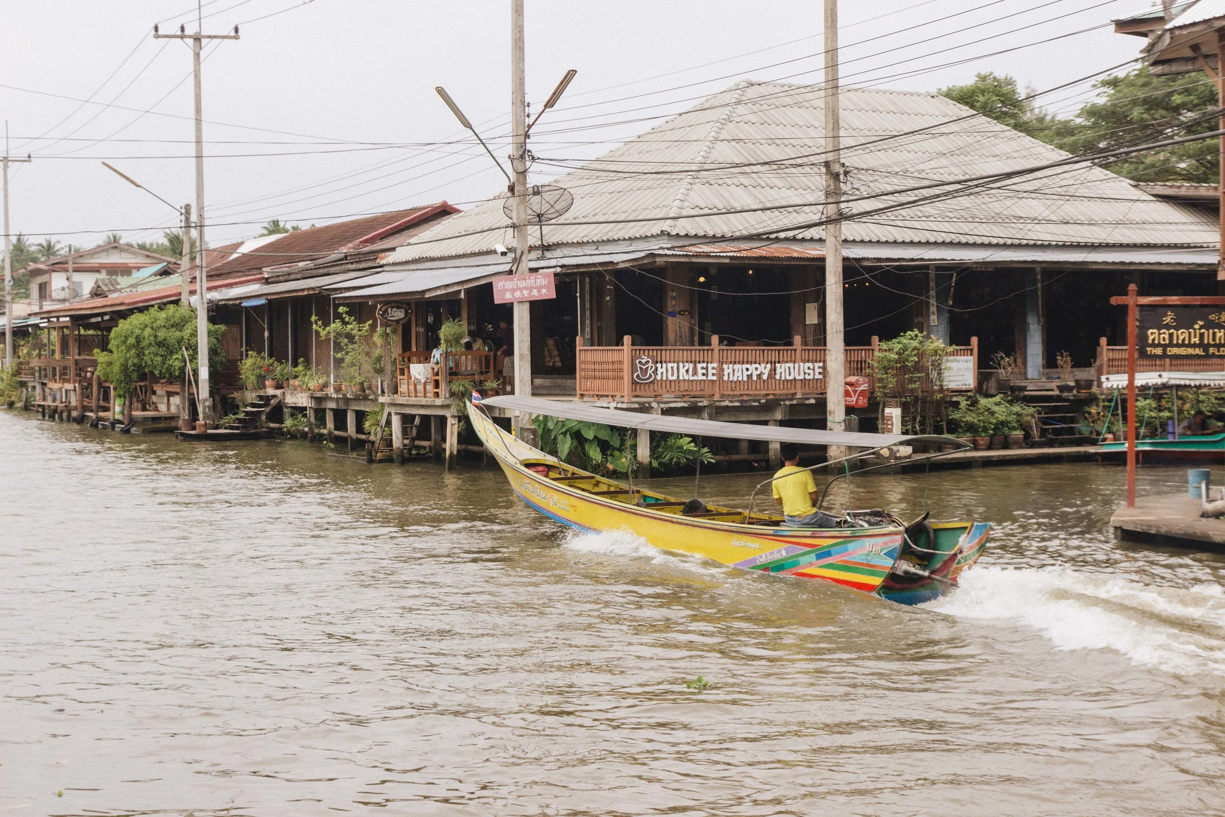 Covered wooden market buildings beside a canal and long-tail boat.