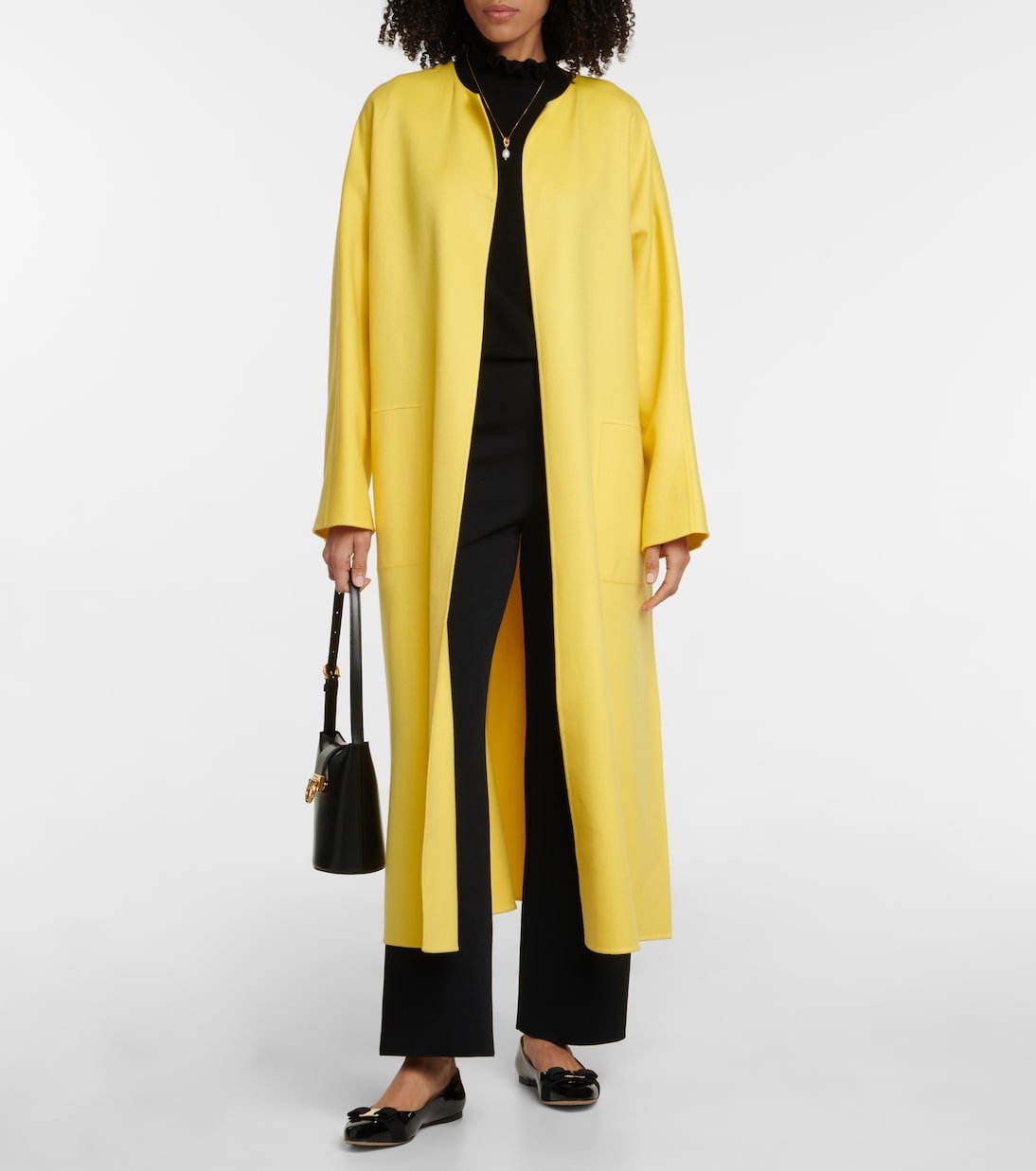 Model wearing black patent-leather ballet flats with black trousers and a long yellow coat.