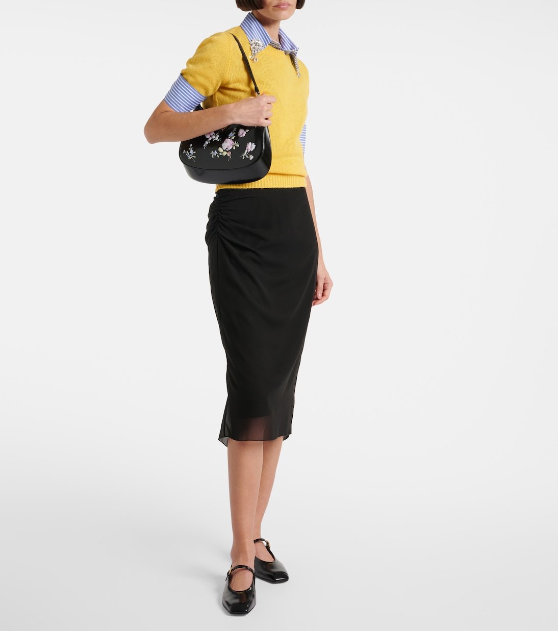 Model wearing black leather Mary Jane flats with a skirt and a yellow knit top.