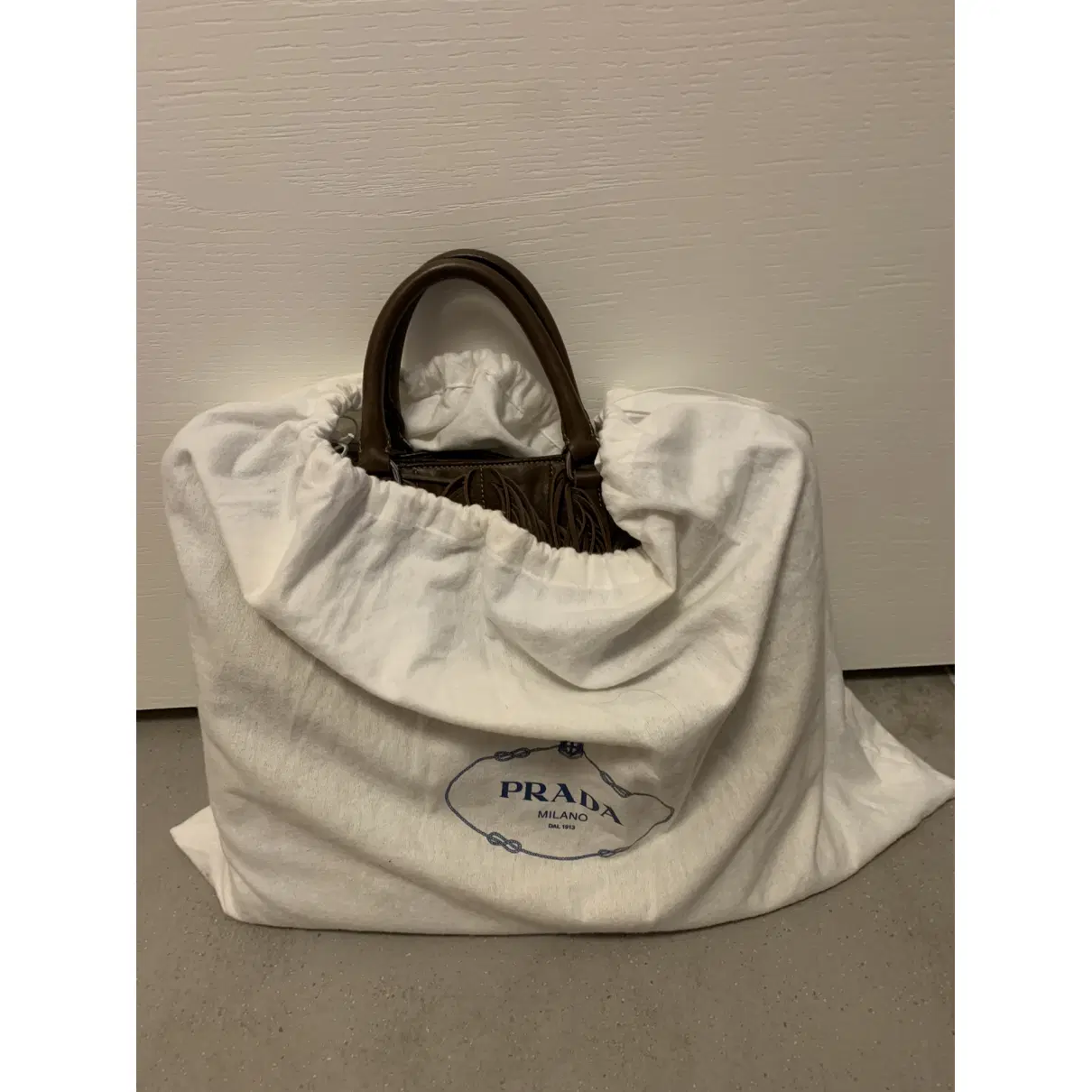 Brown Prada leather handbag stored inside a protective Prada dust bag.