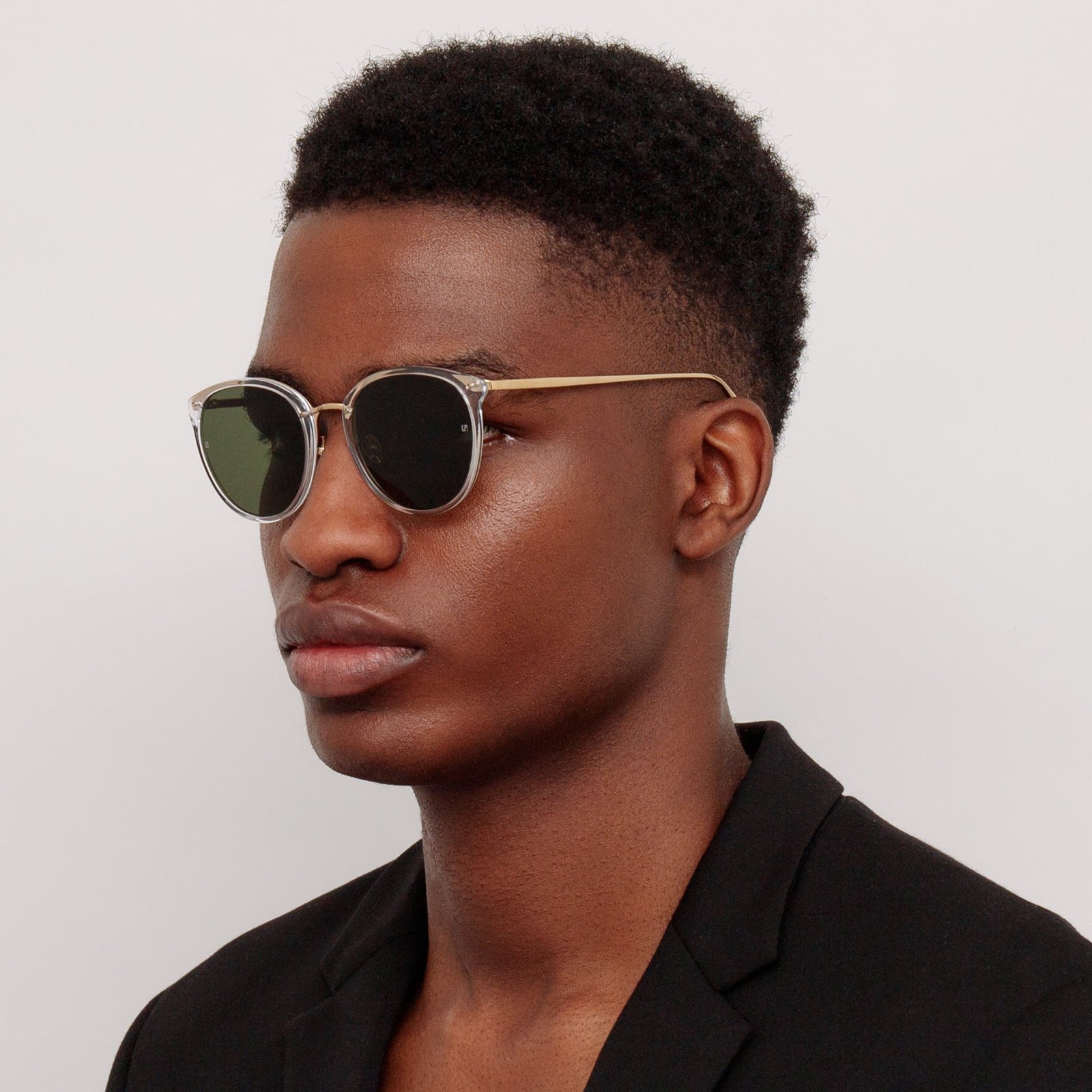 Model wearing Linda Farrow Calthorpe oval sunglasses with a black open-collar shirt.