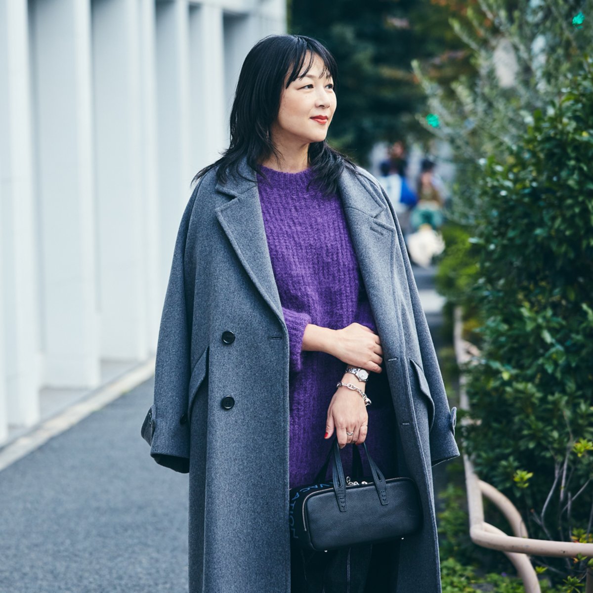 Woman wearing a purple sweater beneath a pale grey coat.