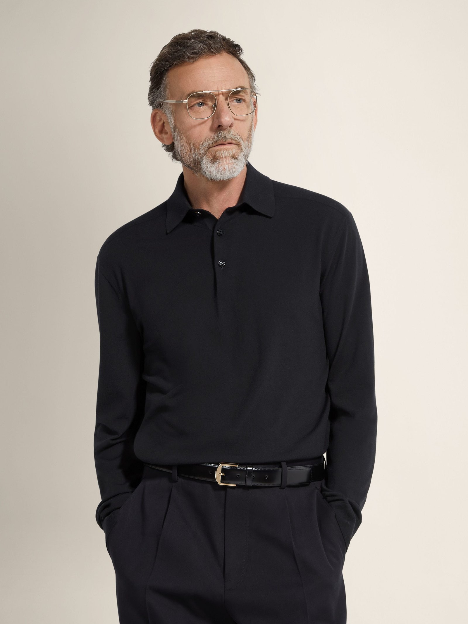 Man wearing a dark fine-knit collared sweater tucked into tailored trousers.
