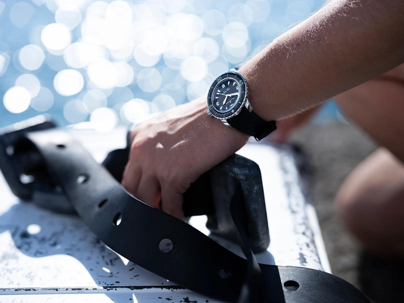 Compact Blancpain Fifty Fathoms Automatique worn on the wrist beside diving equipment.