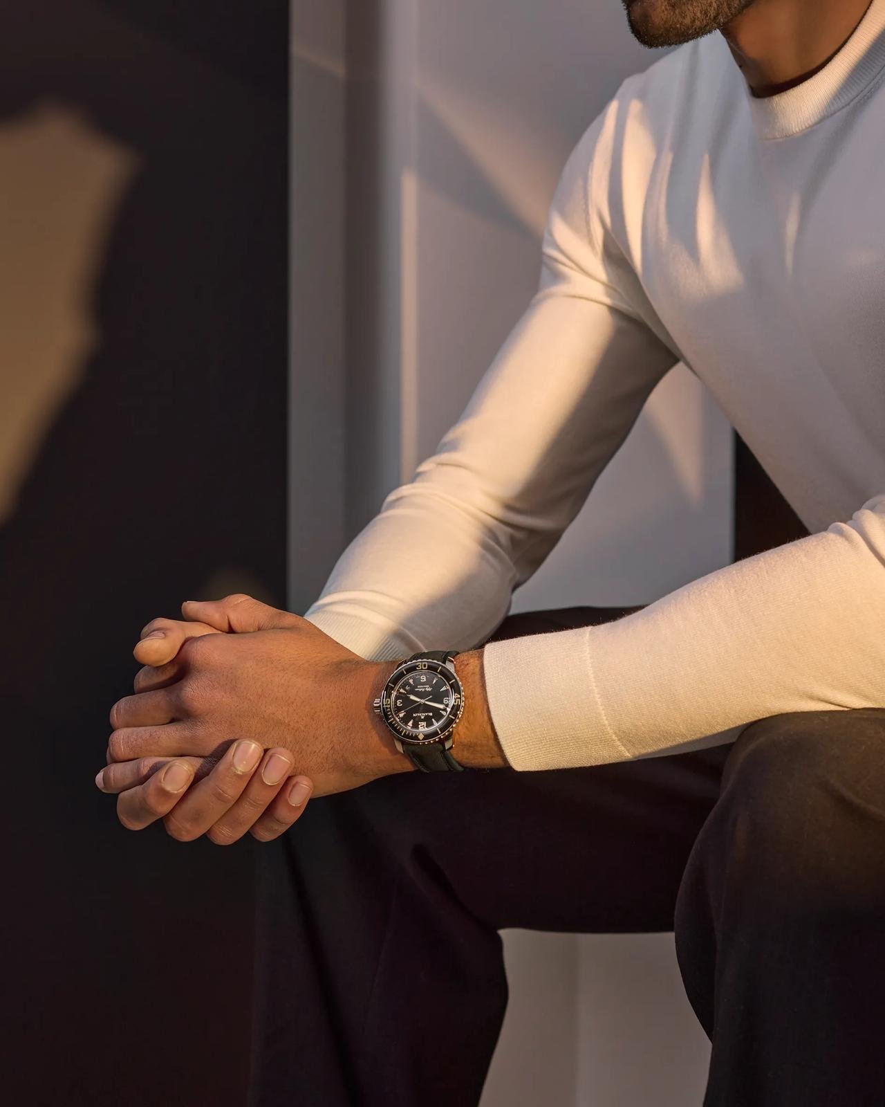 Model wearing a Blancpain Fifty Fathoms with a light long-sleeved knit and dark trousers.