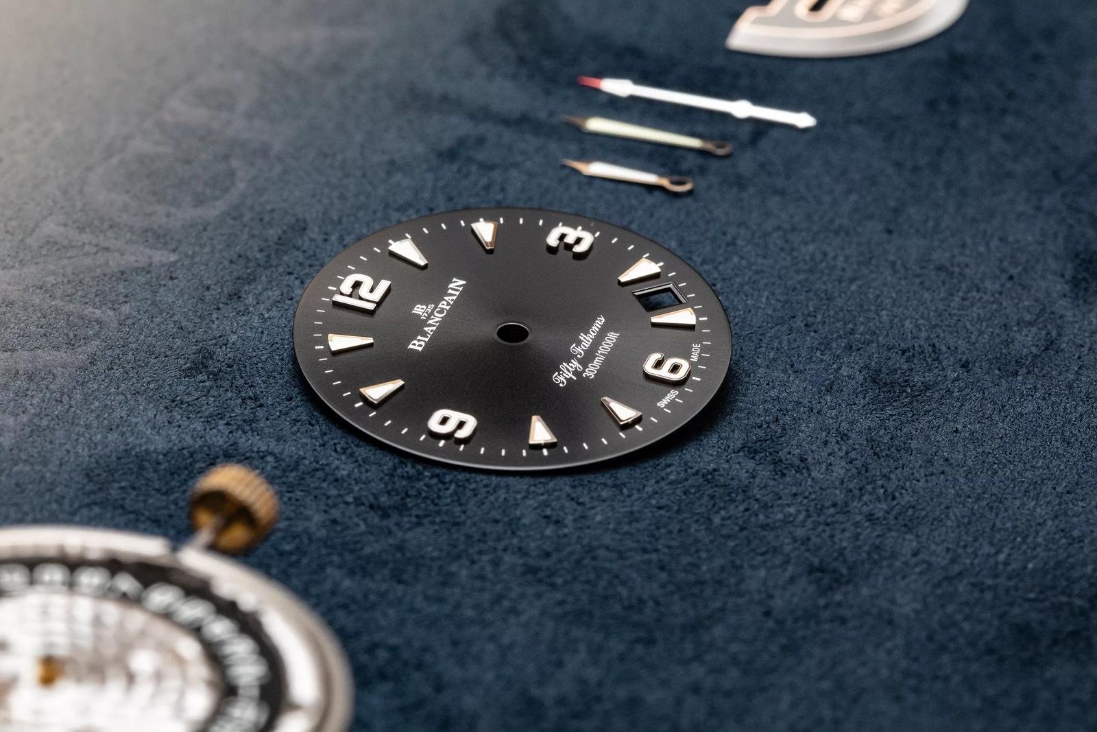 Blancpain Fifty Fathoms dial, hands and movement components on a watchmaking surface.