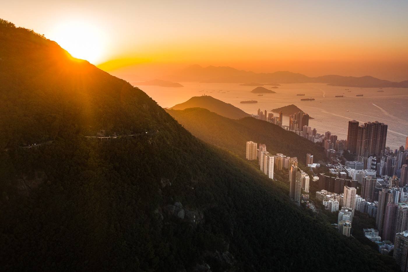 Sunlight over the steep green slopes and city below Victoria Peak.