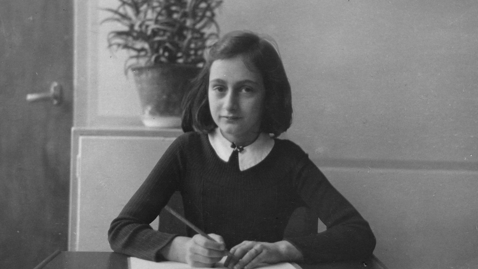 Historical photograph of Anne Frank seated at a desk.